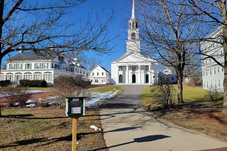 White church with a tall steeple behind a tree-lined walkway in Amesbury, Massachusetts